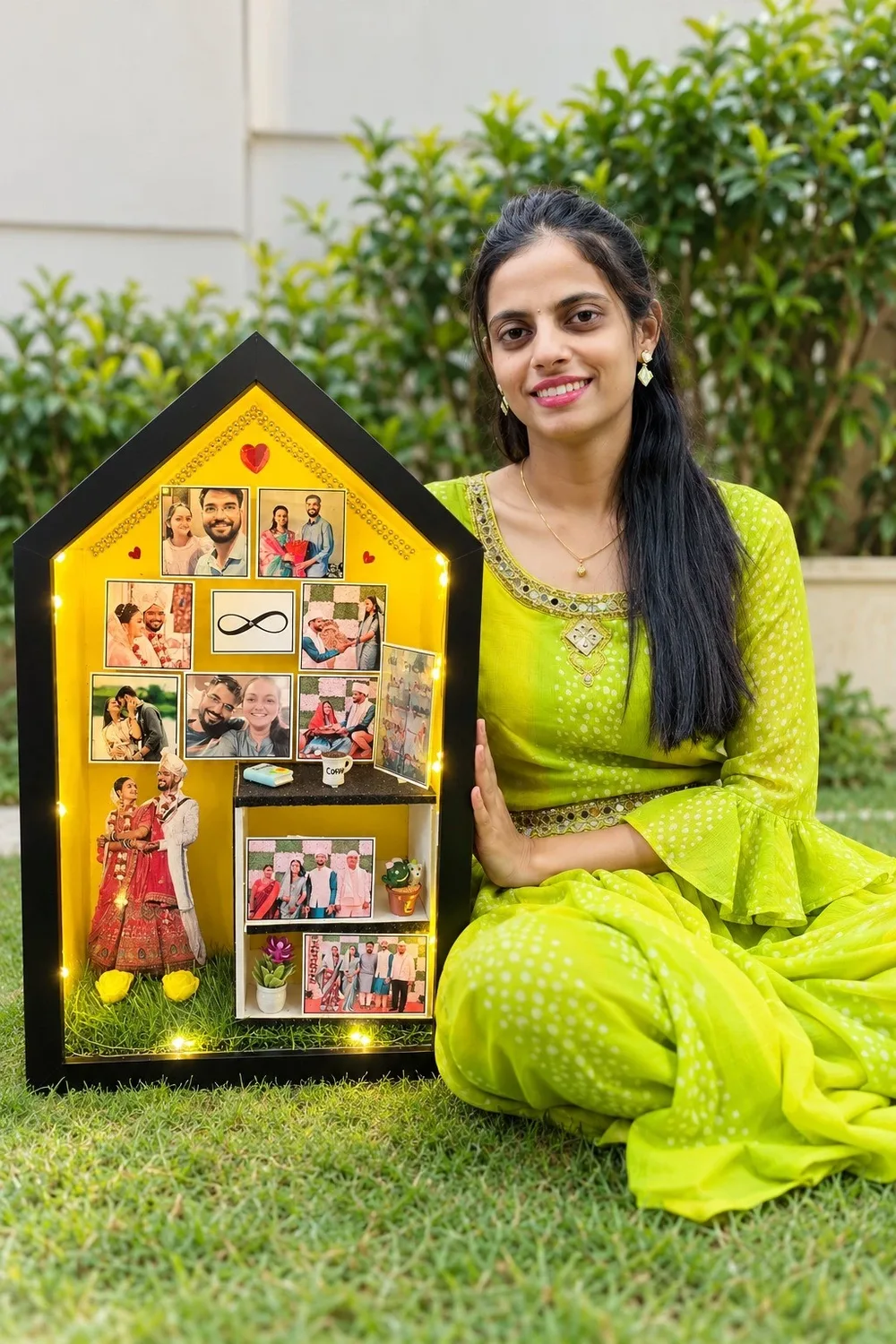 Our maker sitting on the lawn beside a lit, yellow house-shaped miniature frame